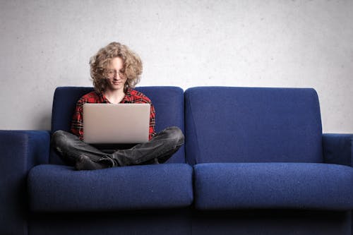 Free Woman in Long Sleeve Shirt Sitting on Blue Sofa Stock Photo