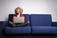 年轻人坐在蓝色沙发上使用笔记本电脑，展现了室内远程工作的生活方式