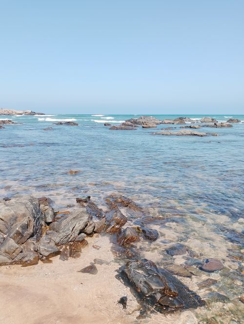 Free A serene rocky beach scene with clear blue water and gentle waves under a bright sky. Stock Photo