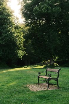 Tranquil park bench under lush green trees during golden hour in Denmark's serene park setting.
