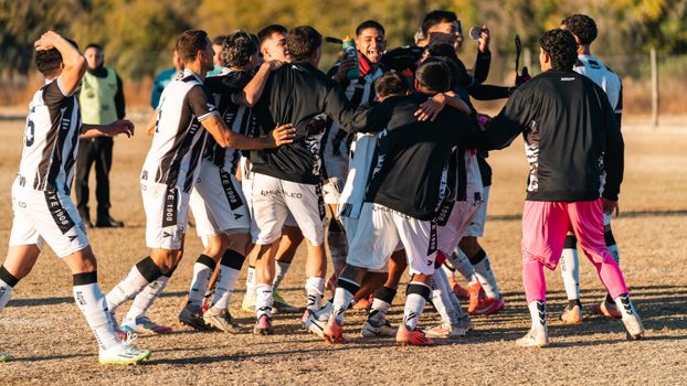 A group of soccer players celebrating a victory on the field in daylight, showcasing team spirit and joy.