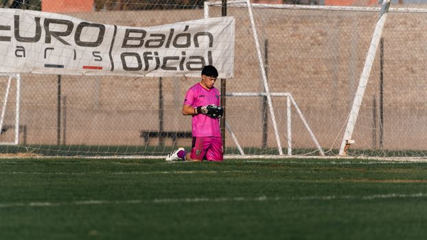 Young soccer goalkeeper in pink gear kneeling on the field during practice.