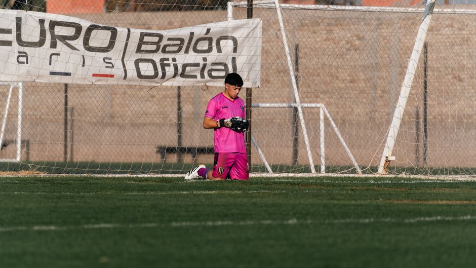Young soccer goalkeeper in pink gear kneeling on the field during practice.