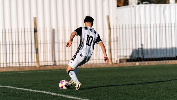 Teenage soccer player in action on outdoor sports field during day.