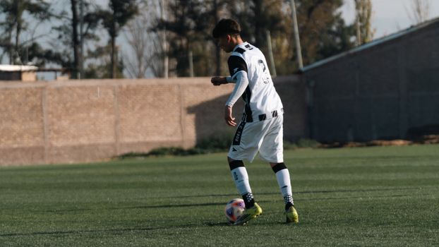 A young male soccer player in action on a green outdoor field during the day.