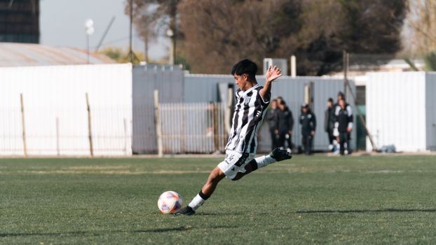 A young soccer player in black and white uniform kicking a ball on an outdoor field.