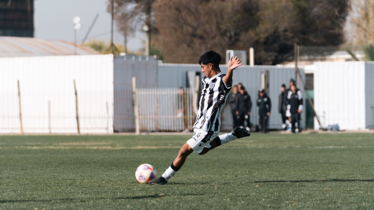 a young soccer player in black and white uniform kicking a ball on an