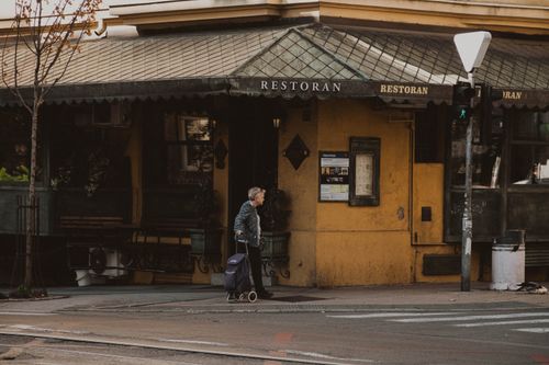 Free An elderly woman with a trolley bag passes by a rustic restaurant in Belgrade, Serbia. Stock Photo