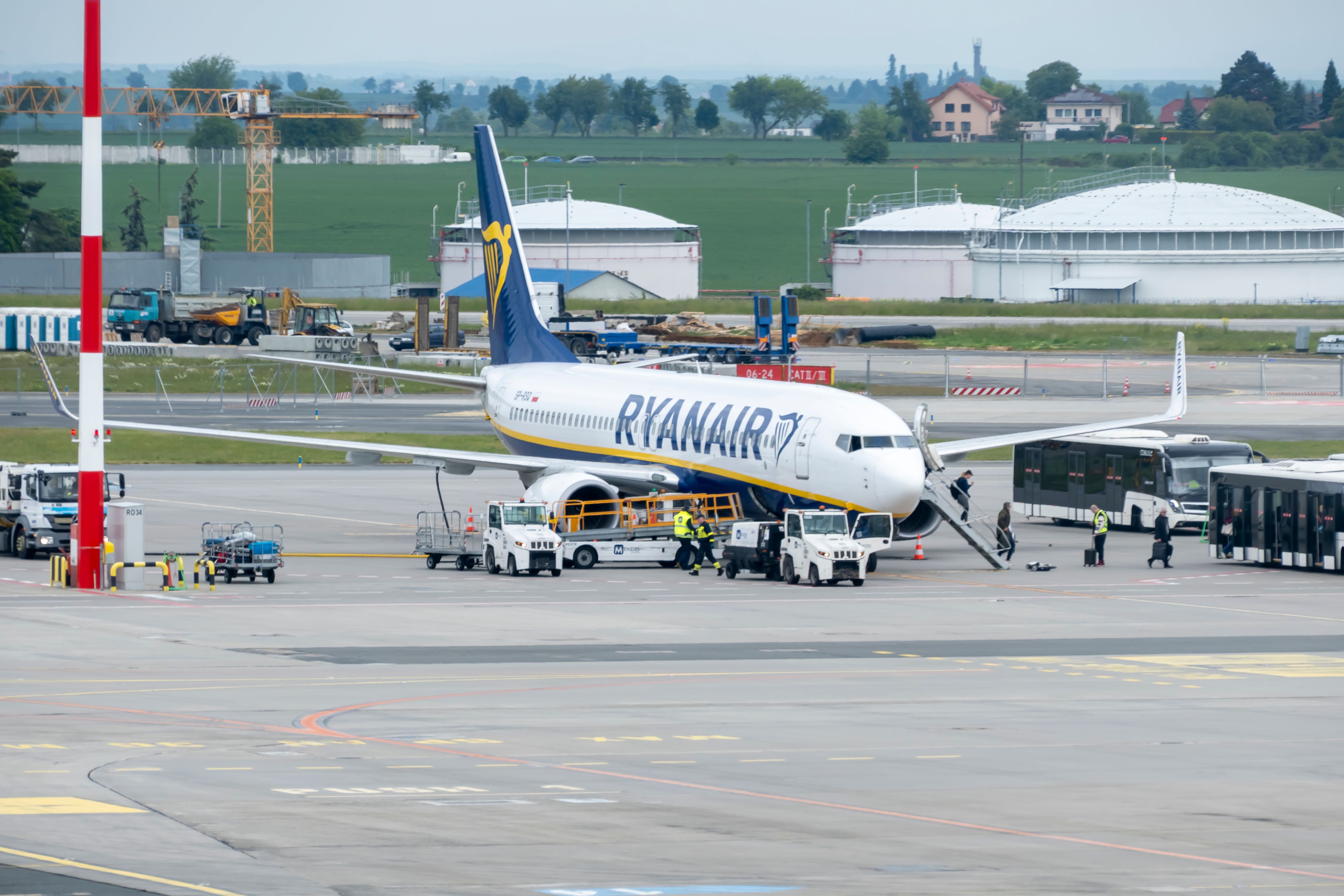 Ryanair aircraft parked on an airport apron with ground crew, service vehicles and passenger buses