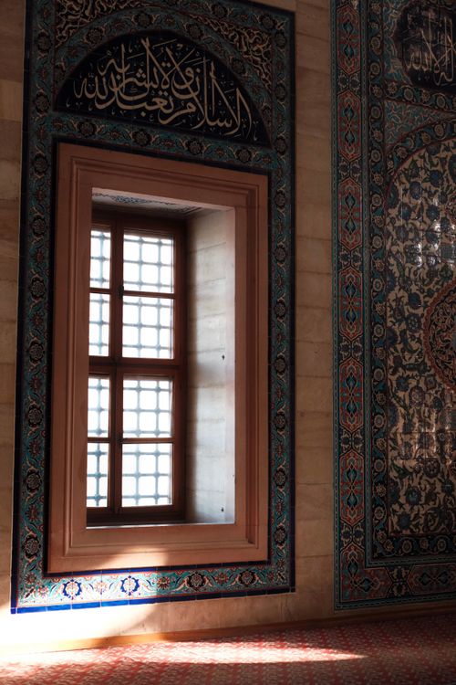 Free Sunlight illuminates an ornate Islamic window, highlighting intricate tile patterns in an ancient interior. Stock Photo