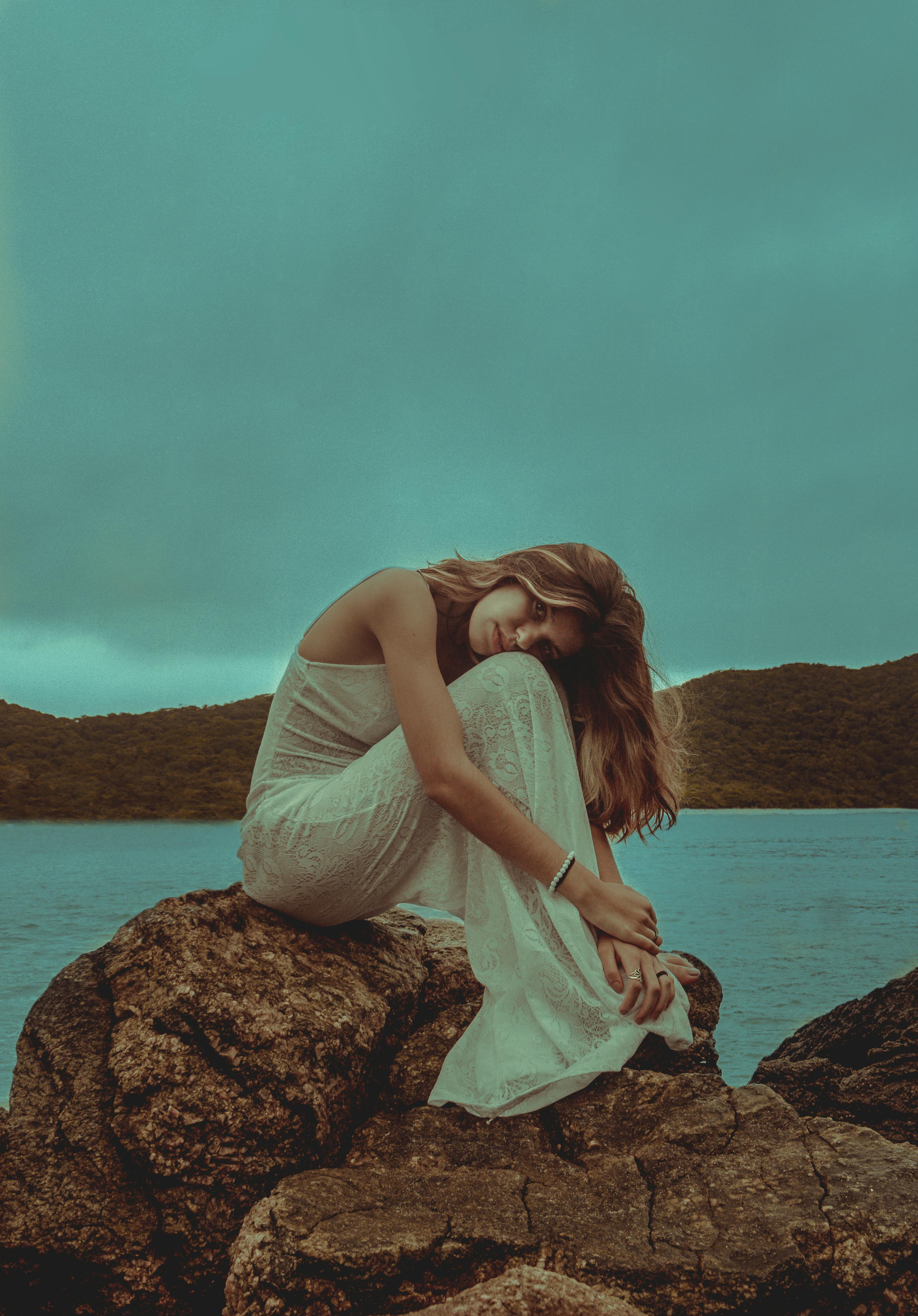 一名女子身穿白色连衣裙，在巴西海边的岩石上摆姿势