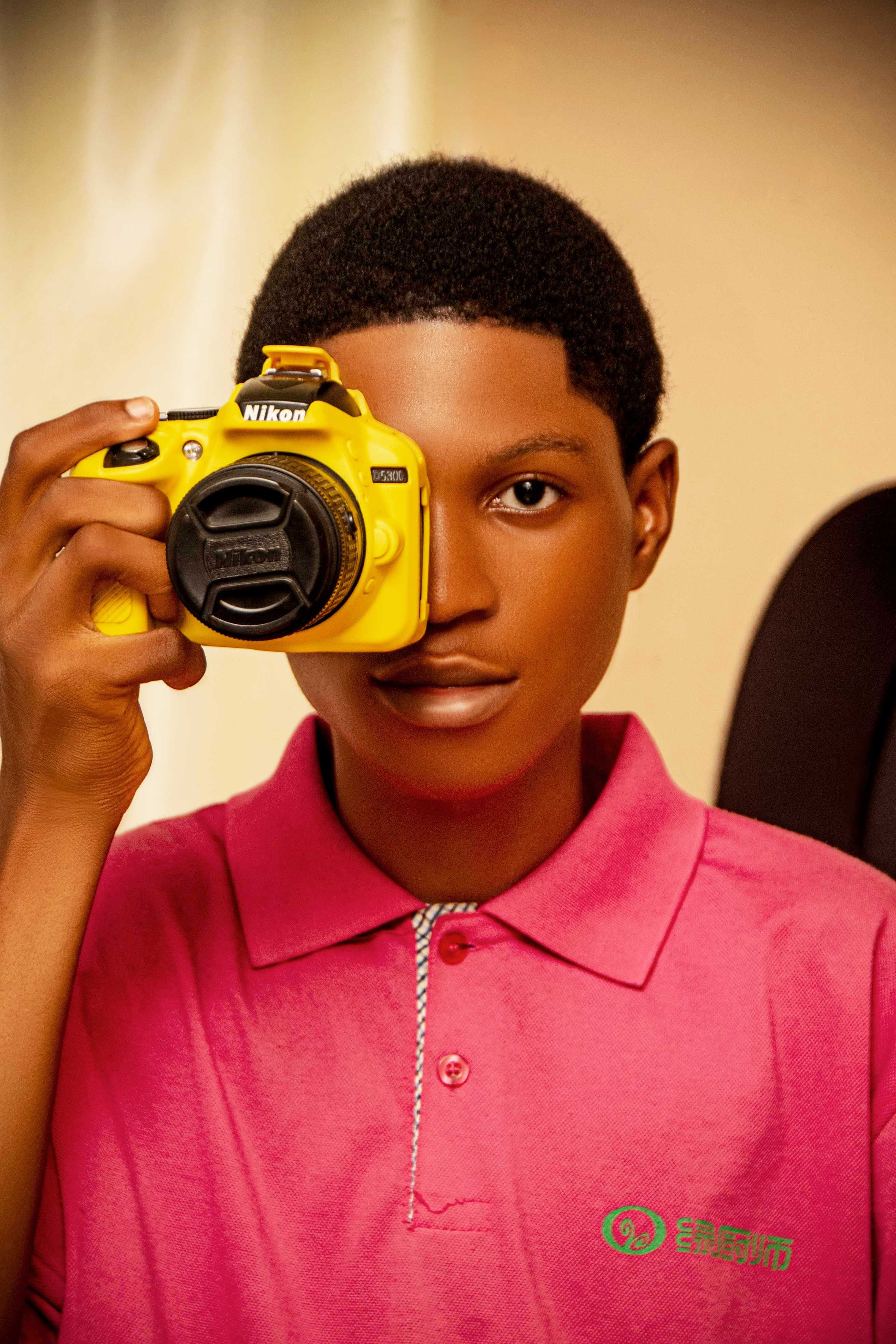 A teenager poses with a yellow camera, capturing a creative portrait.