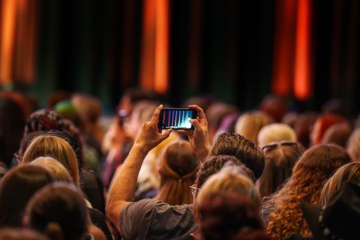 A crowd enjoys a live performance, recording on a smartphone at an indoor concert.