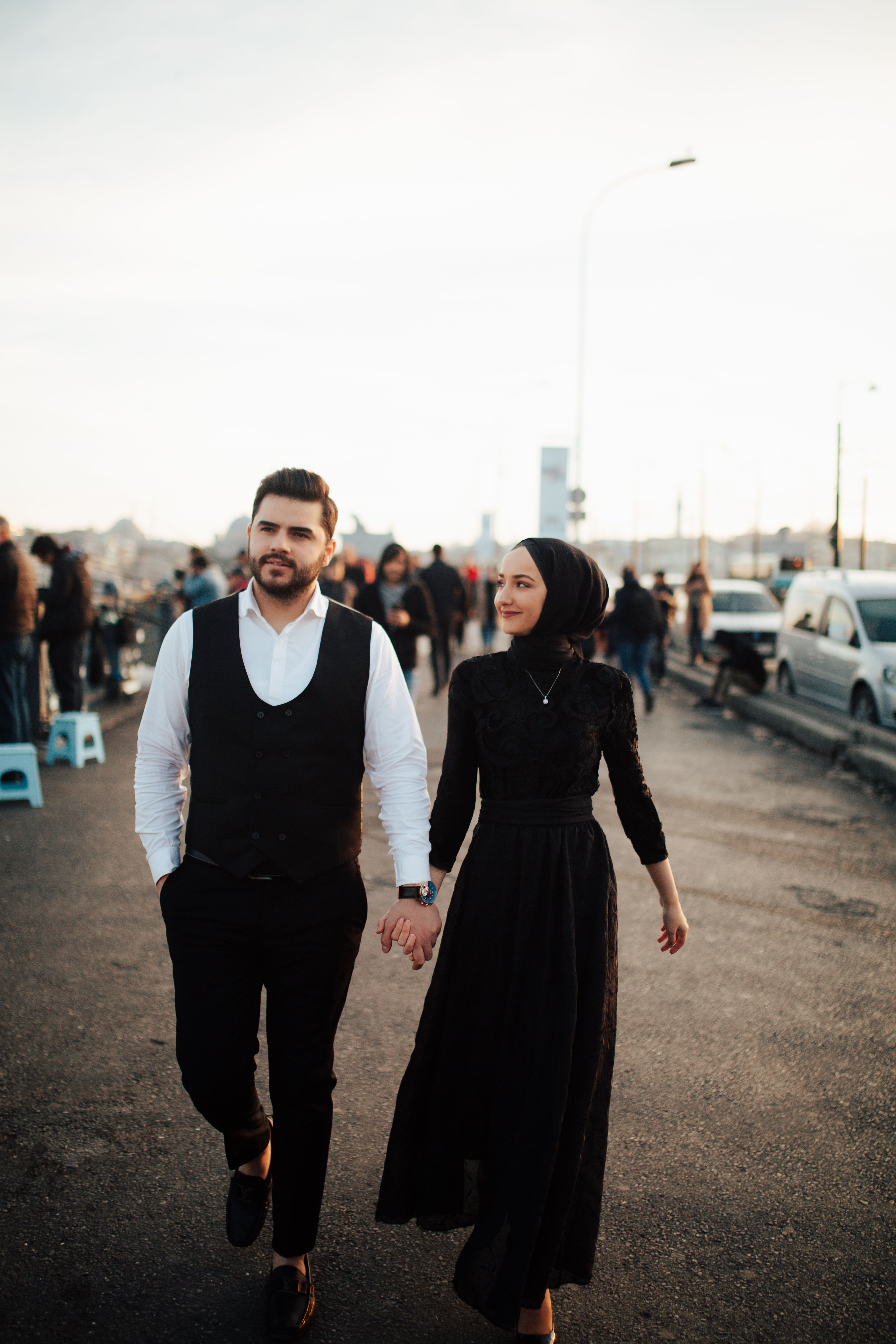 A couple strolls in İstanbul, Türkiye, holding hands at sunset on a busy street.