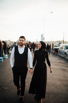 A couple strolls in İstanbul, Türkiye, holding hands at sunset on a busy street.