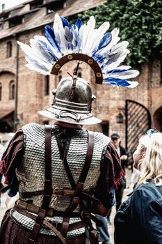 Back view of a medieval knight with feathered helmet at a historical event.