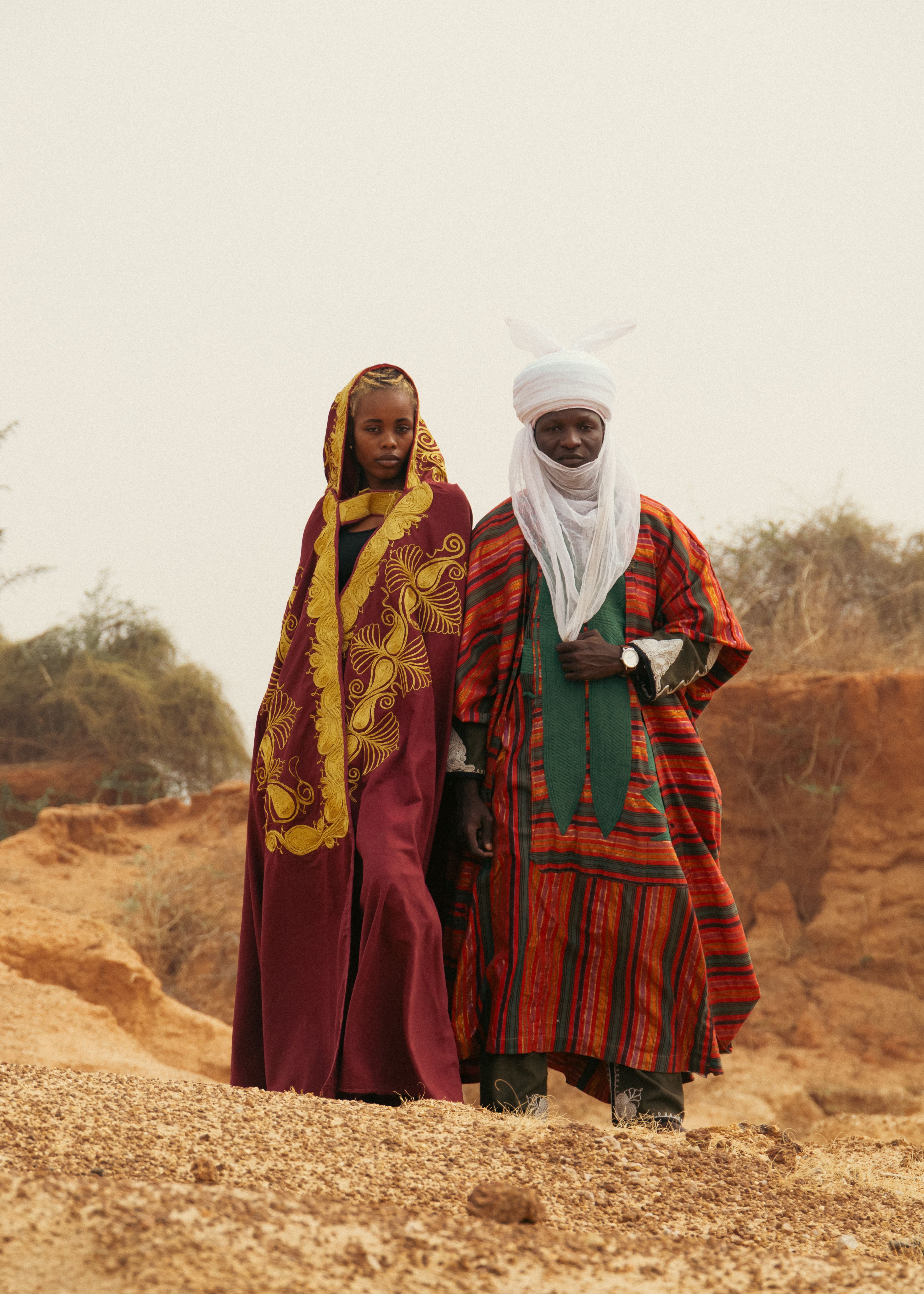 Elderly couple in vibrant traditional African clothing standing in a desert landscape.