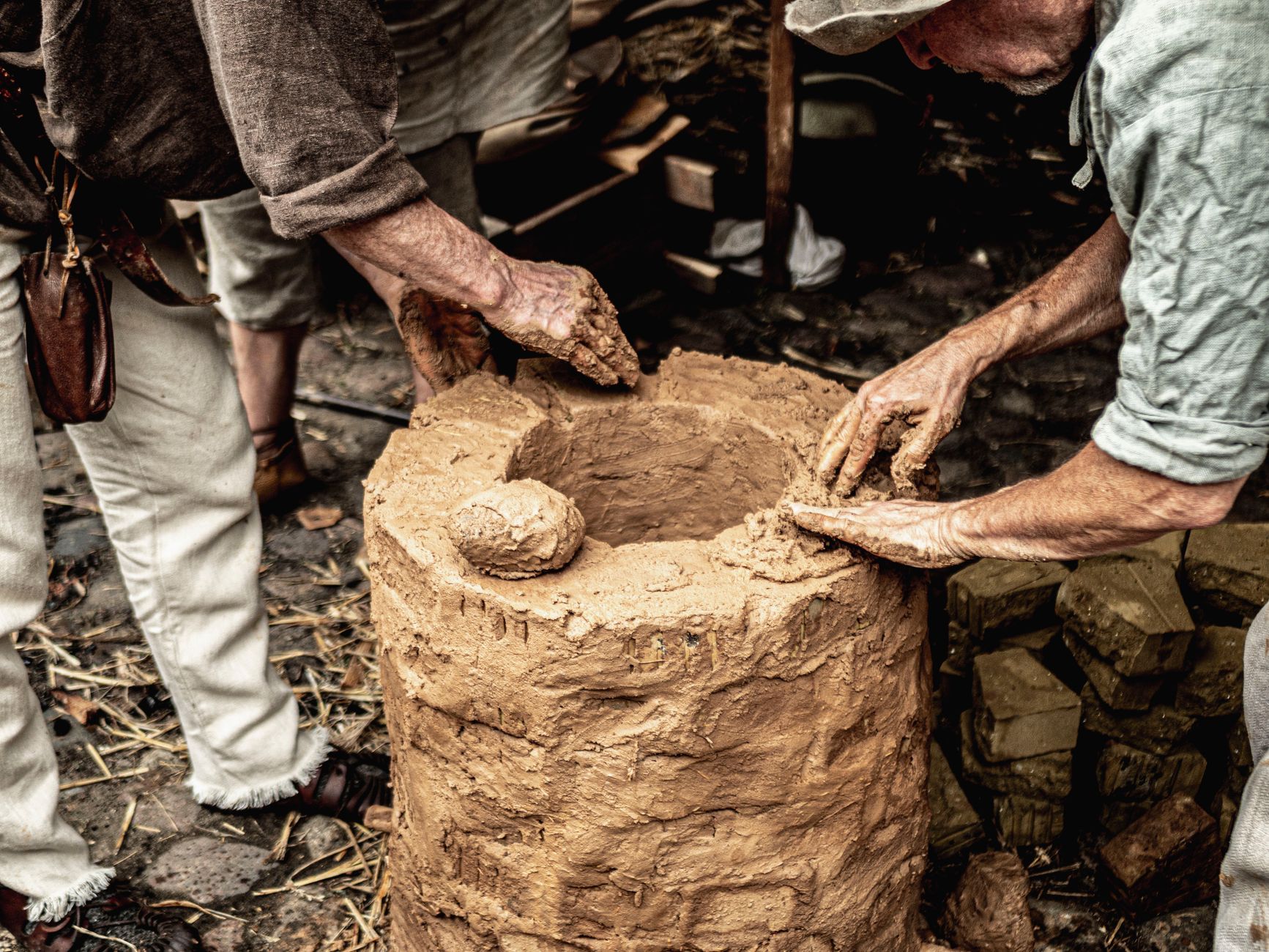Hands crafting a clay oven outdoors, showcasing traditional methods and teamwork.