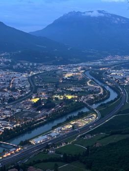 Panoramic aerial view of Trento cityscape and mountains at dusk, highlighting Adige River.