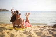 一位戴着太阳镜的女人在海滩上享受夏日的微风和阳光，晒着日光浴