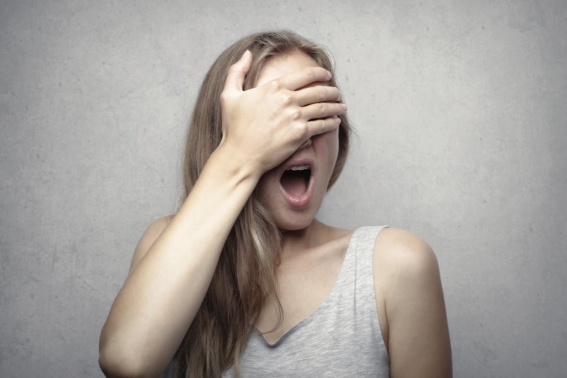 Free Woman in Gray Tank Top Covering Her Face With Her Hand Stock Photo