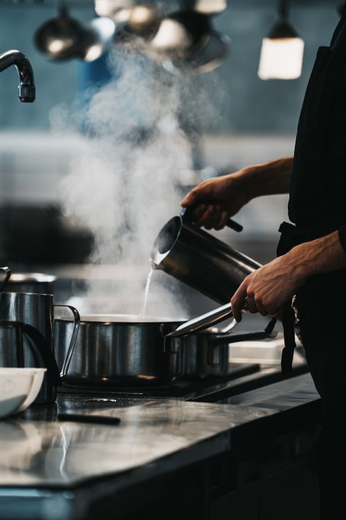 Free A chef skillfully pours water into a steaming pot in a professional kitchen, creating an inviting culinary scene. Stock Photo