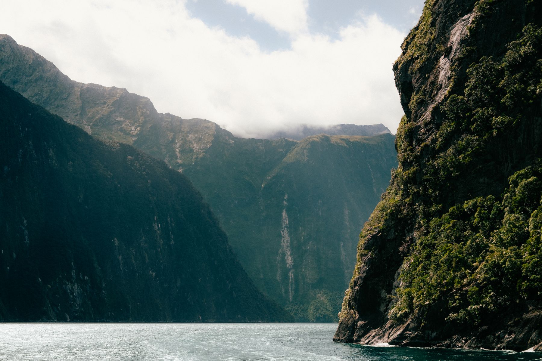 Boat beneath the forested cliffs and waterfalls of Milford Sound / Piopiotahi
