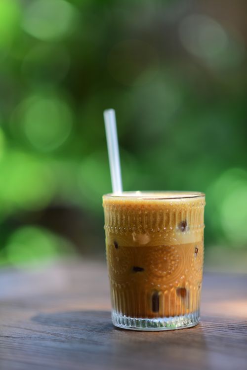 Free Close-up of iced coffee in a decorative glass with a straw, against a blurred green background. Stock Photo