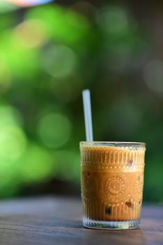 A close-up of iced coffee in a beautifully textured glass with a straw, set against a blurred green background.