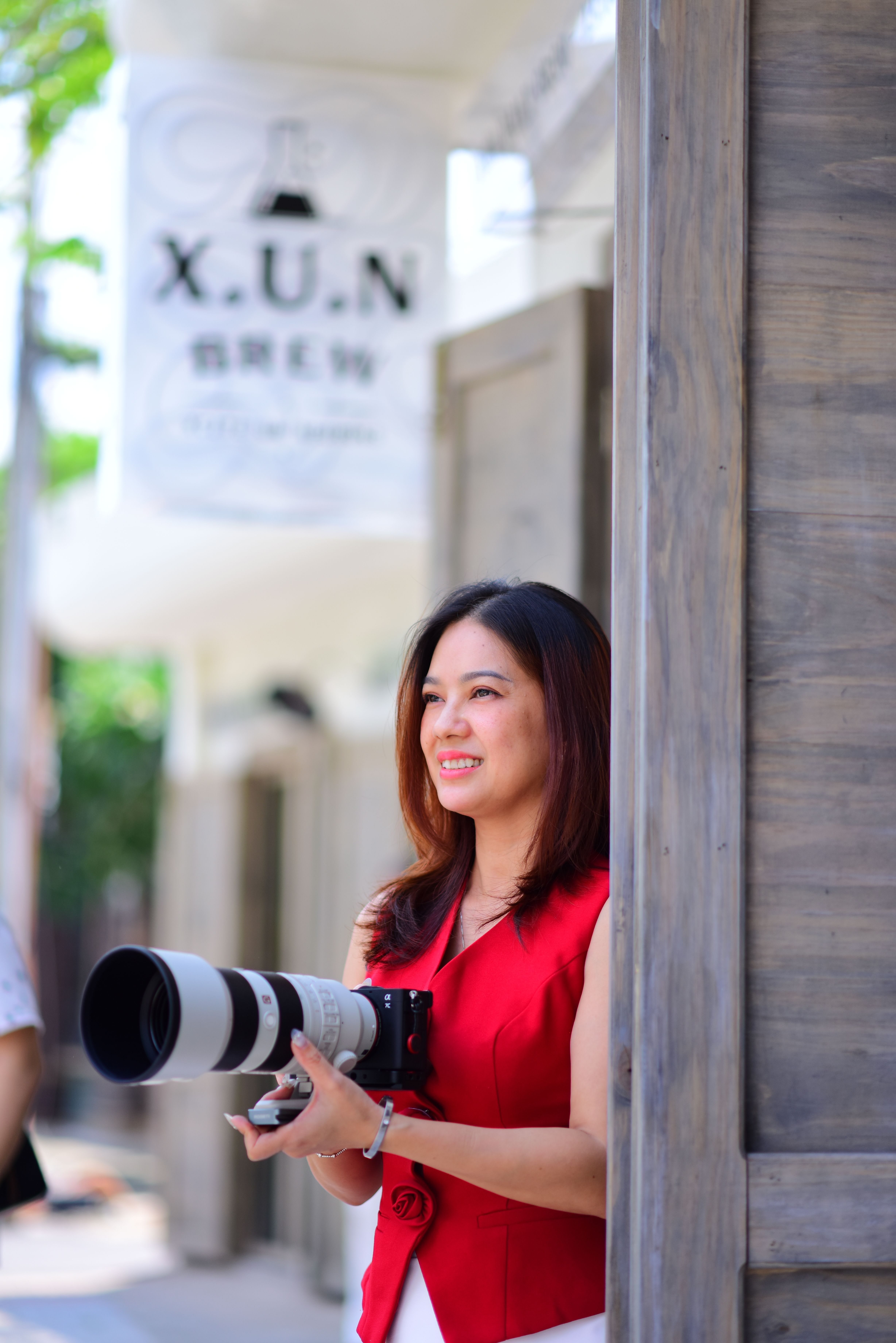 Professional female photographer captured outdoors holding a telephoto lens, exuding confidence and focus.