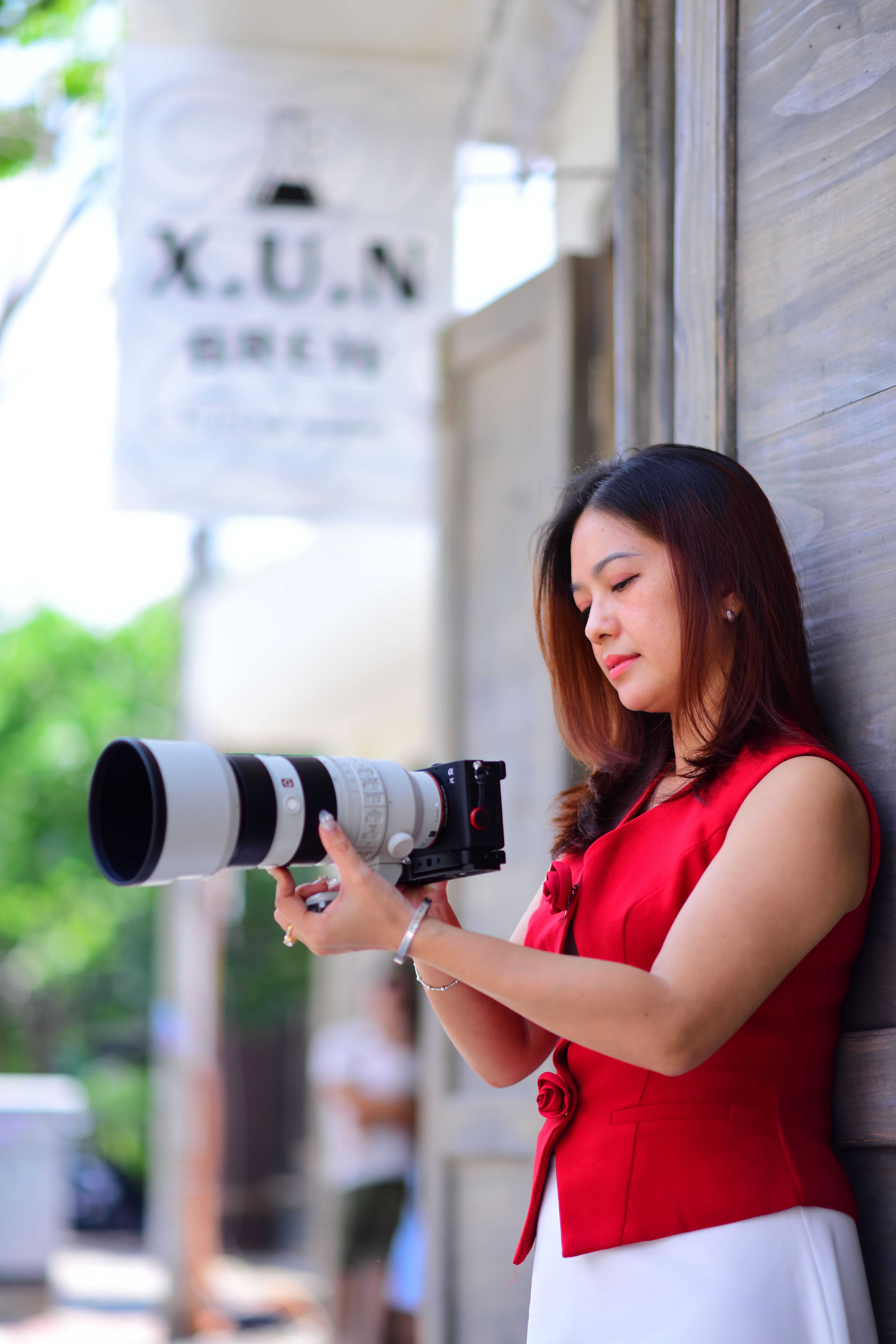 Woman photographer using a large telephoto lens outdoors in a sunny setting, appearing focused and professional.