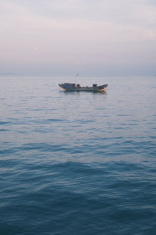 Free Tranquil scene of a solitary fishing boat on calm waters during dusk in Vietnam, reflecting serenity. Stock Photo