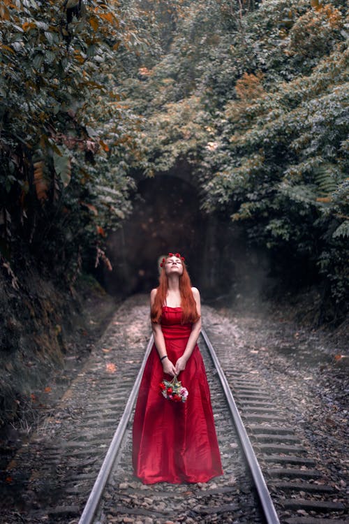 기차 트랙에 서있는 빨간 드레스 여자