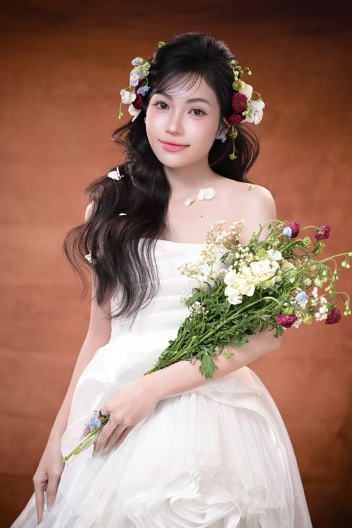 Free A beautiful bride in a white dress holding a bouquet, adorned with a floral headpiece on a warm backdrop. Stock Photo