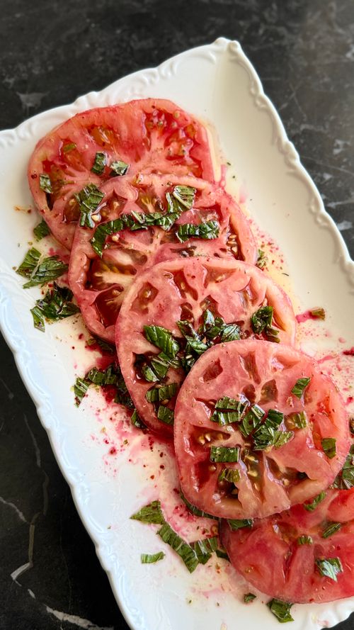 Free Sliced heirloom tomatoes garnished with fresh herbs on a decorative platter. Stock Photo