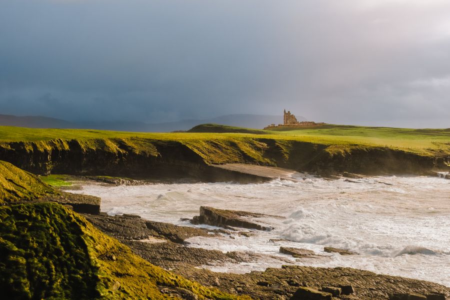 View of Classiebawn Castle atop coastal cliffs in County Sligo, Ireland, with waves crashing below