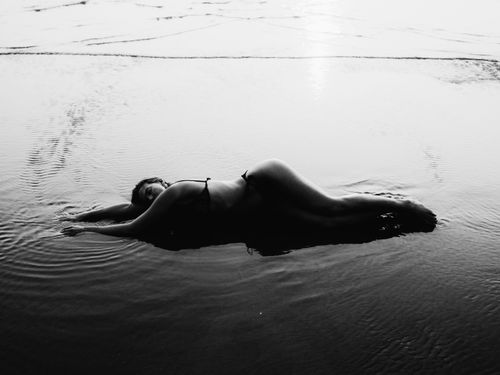 Free Artistic black and white image of a woman laying in shallow water at the beach during the day. Stock Photo