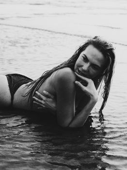 Artistic black and white portrait of a woman relaxing on a beach in shallow water.