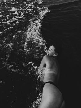 Artistic black and white photo of a woman at the beach enjoying the ocean waves.