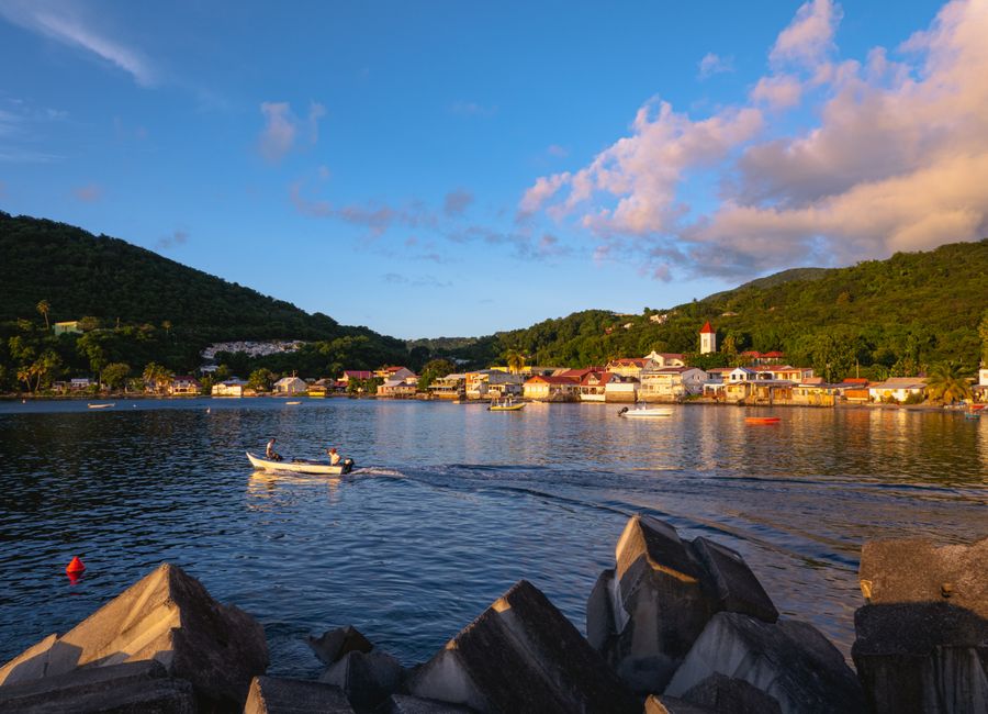 A picturesque sunset over Deshaies Bay, Guadeloupe, with a small boat in the foreground.