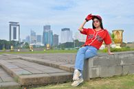Woman in trendy casual outfit poses with Jakarta skyline in the background, showcasing modern urban fashion.