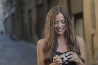 黑发女子在城市环境中愉快地使用老式相机，微笑着