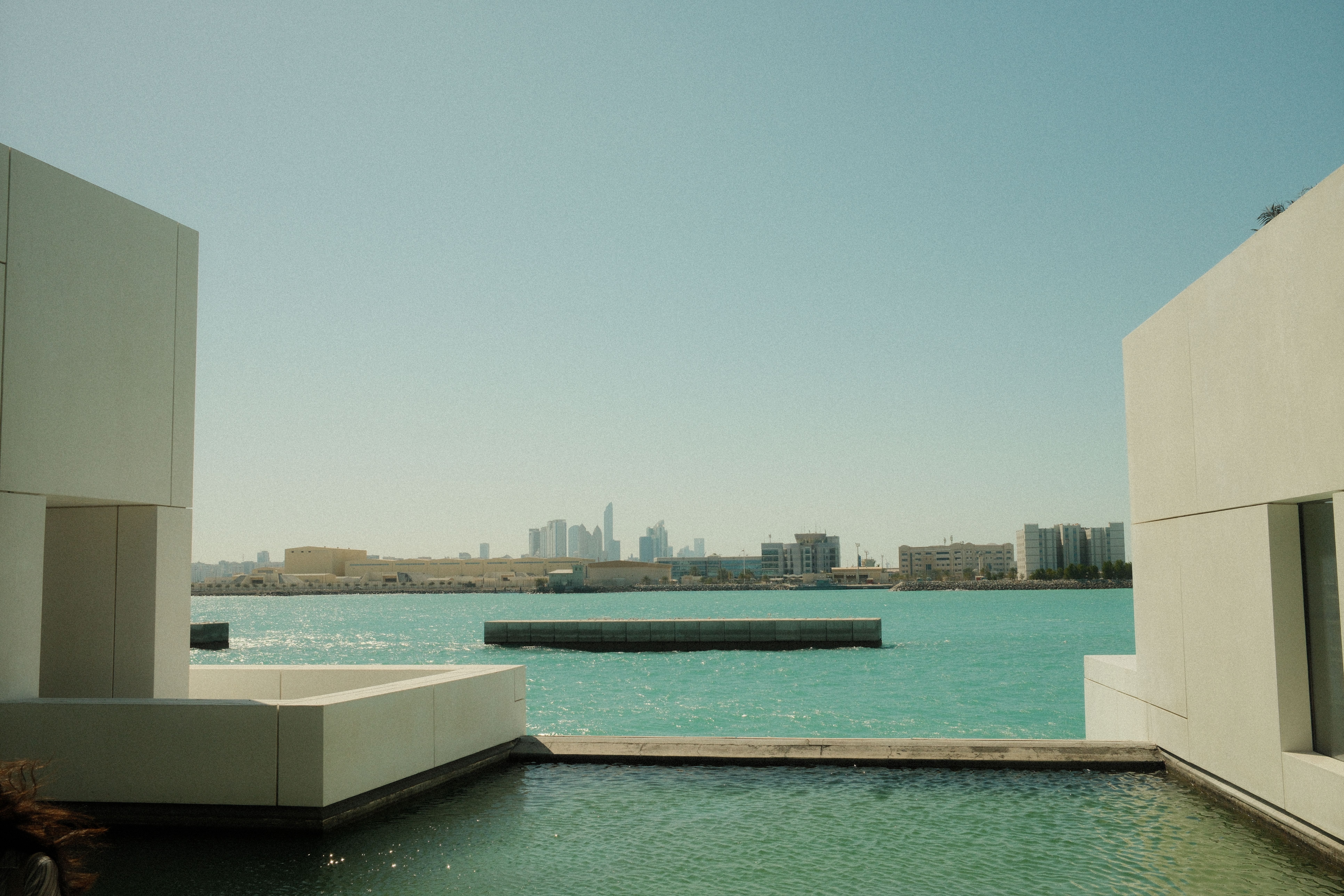 Elegant waterfront architecture framing a distant city skyline across blue waters.