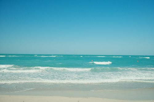 Free Tranquil sandy beach with gentle ocean waves under a clear blue sky. Stock Photo