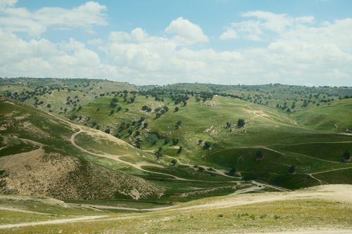 Free A scenic view of rolling green hills under a bright blue sky with white clouds. Stock Photo