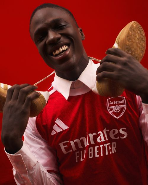 Free Joyful man in Arsenal jersey with football cleats, smiling pose. Stock Photo
