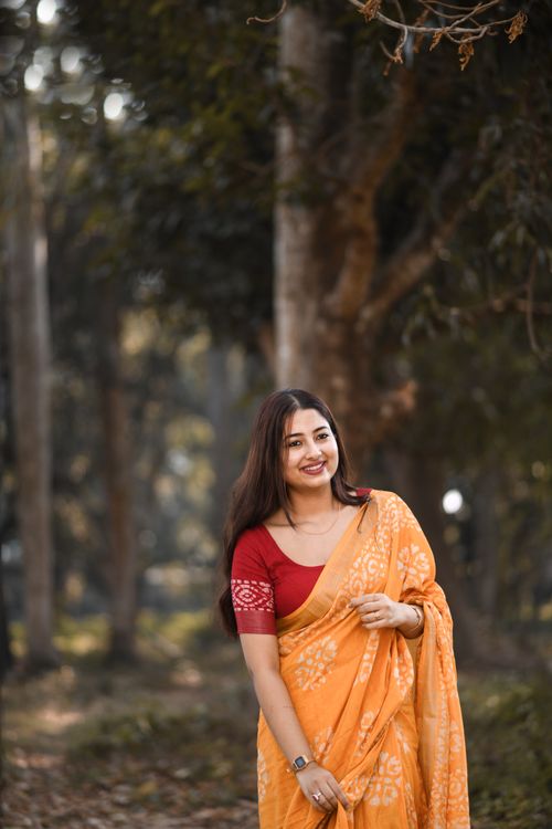 Free A woman wearing a yellow saree stands smiling amidst a forest setting, exuding warmth and joy. Stock Photo