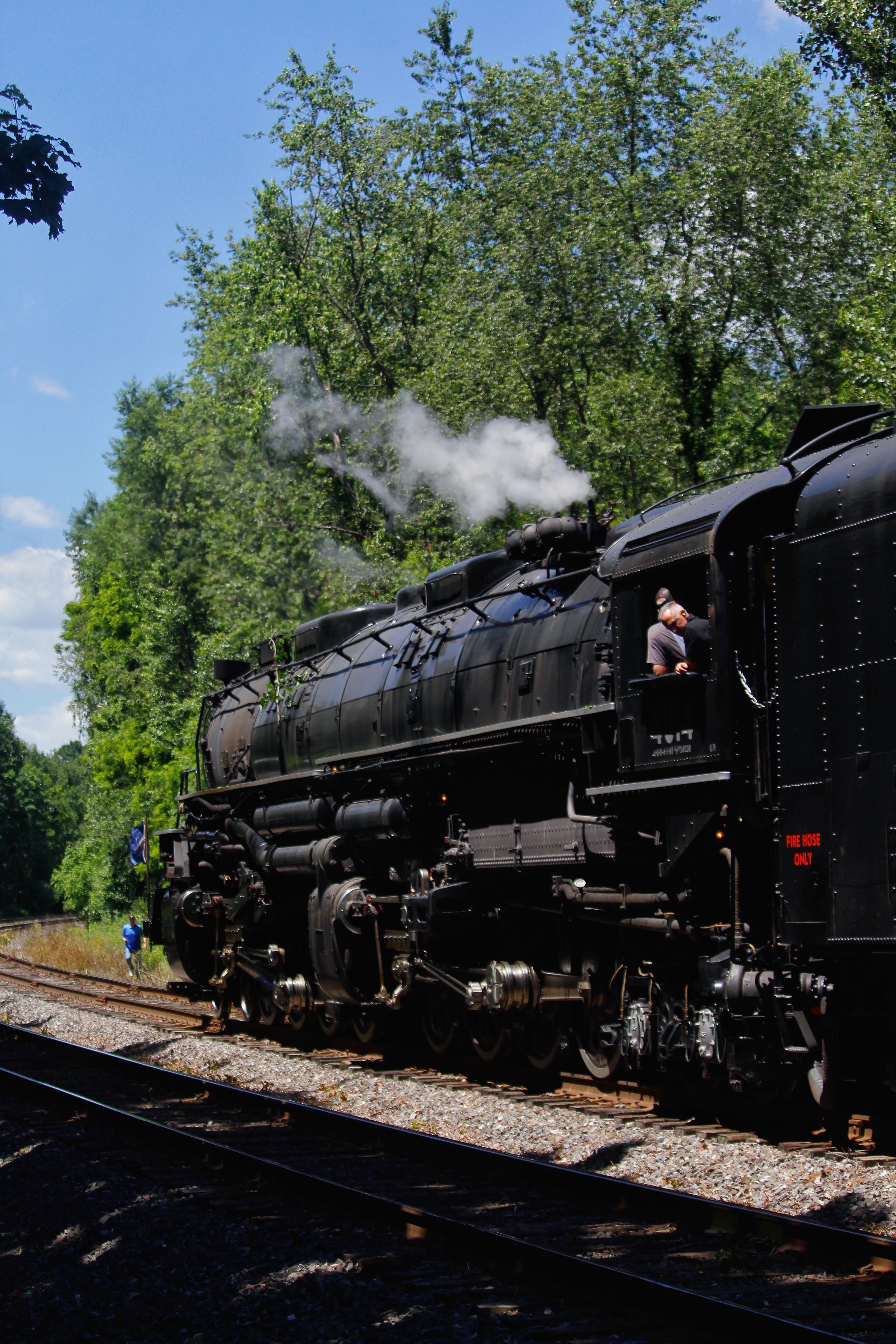 A classic steam locomotive emits smoke as it travels through lush greenery.