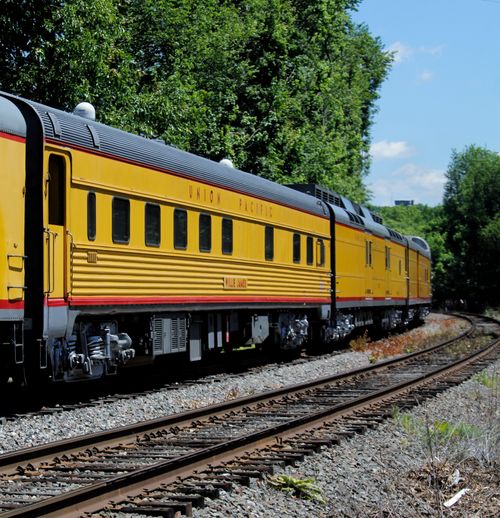 Free Yellow Union Pacific train traveling on tracks through lush summer landscape. Stock Photo