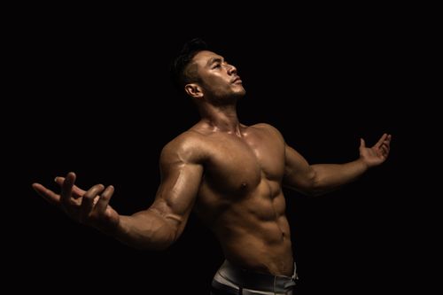 Free Muscular male model posing confidently in a dramatic lighting environment, showcasing fitness and strength. Stock Photo